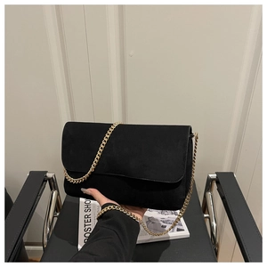 Detail showing hand holding black suede square bag with elegant gold chain strap