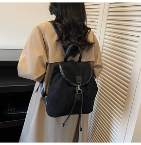 Detail of a matte black backpack featuring leather trim and drawstring on a female model