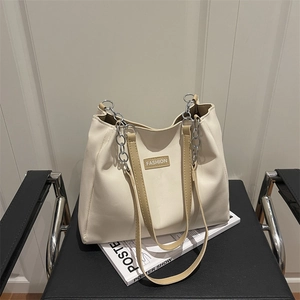 Minimalist beige tote bag with khaki leather straps and fashion label on a leather chair