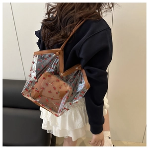 Detail of transparent cherry print tote bag with leather straps on model shoulder
