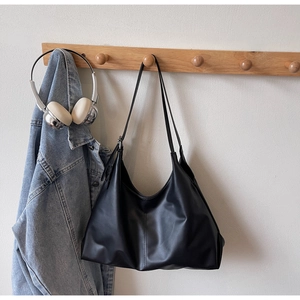 Close-up of a black minimalist hobo tote bag hanging on a light wood rack with denim jacket