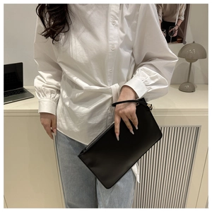 Close-up of a minimalist black zip wristlet clutch held by a model in a modern office set
