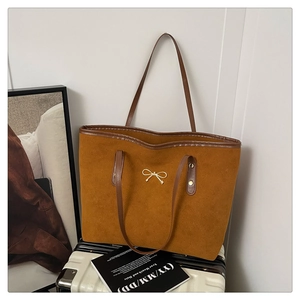 Close-up of caramel suede tote bag with gold bow buckle on a white suitcase