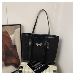 Detail of a minimalist black suede tote bag featuring a small golden bow accent