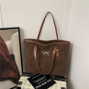 Sac cabas en daim marron avec nœud doré posé sur une valise blanche décor d'automne