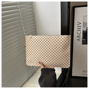 Detail of a creamy white textured clutch bag with reddish monogram and gold zipper closure