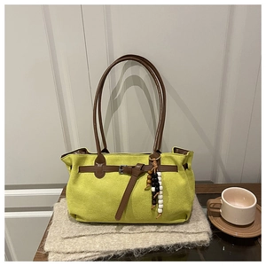 Detail of green suede tote bag with brown leather straps and colorful beaded charm