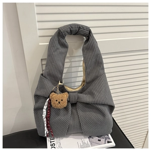 Gros plan du sac cabas en velours côtelé gris avec grand nœud et breloque ours en peluche