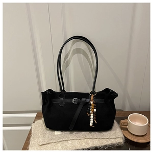 Close-up of black suede tote bag with metal buckle and ethnic beaded charm on wood table