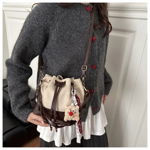 Detail of beige drawstring bucket bag with brown leather base and cute plush bear charm