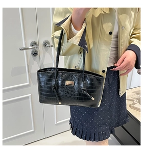 Detail of black crocodile texture tote bag featuring a gold metal nameplate and knotted handle