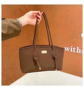 Detail of dark brown quilted leather tote bag featuring a metallic logo and knotted handles