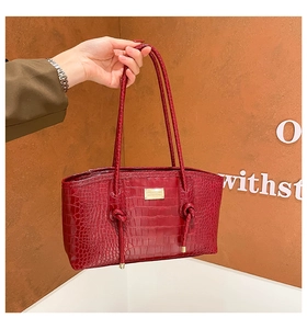 Detail of red crocodile embossed tote bag featuring gold logo plate and knotted strap design