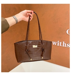 Detail of dark brown croc-pattern tote featuring knotted strap and gold logo plate