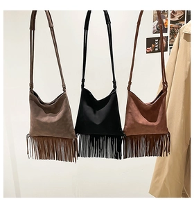 Trois sacs à bandoulière en daim avec de longues franges sur un mur minimaliste