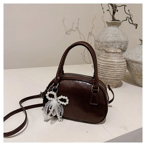 Close-up of retro coffee brown handbag with pearl lace bow charm and smooth PU texture