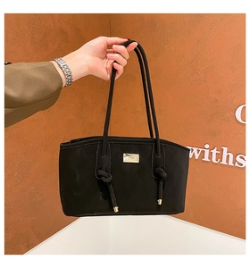 Detail of black quilted handbag with golden logo plaque and elegant knotted handles
