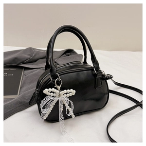 Detail of black bowling handbag with white lace pearl bow charm on gray blazer background