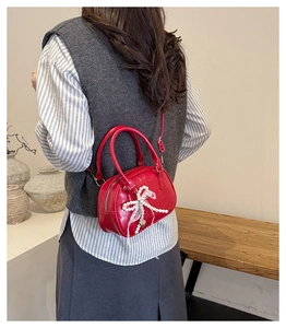 Detail of red leather bag with pearl lace bow charm worn by a model in a natural setting