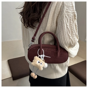 Detail of burgundy faux suede baguette bag with plush charm on beige knit sweater