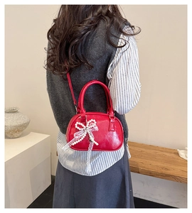 Close-up of a red semi-circular handbag with pearl bow and lace charm detail