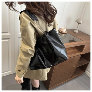 Detail of glossy black tote bag with chain strap shown on khaki trench coat model
