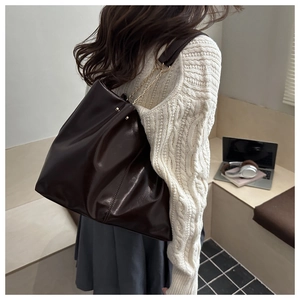 Detail of deep brown large leather tote bag with stylish gold chain strap on shoulder