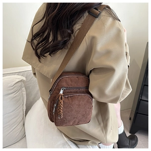 Détail du sac bandoulière en velours côtelé marron avec large sangle et breloque tissée