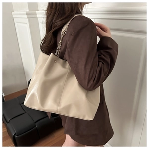 Detail of solid beige tote bag featuring metal chain shoulder strap and vertical stitching