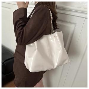 Detail of white glossy tote bag with metal chain strap shown on model shoulder
