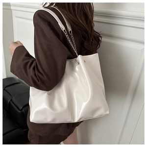 Detail of glossy white tote bag with golden chain strap and rivets on a blazer