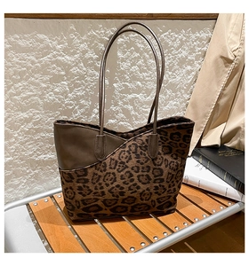 Detail of leopard print tote bag with brown leather trim and V-shaped top on wooden bench