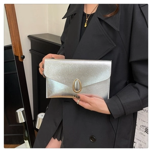 Close-up of silver envelope clutch with metallic texture and gold buckle held by a model
