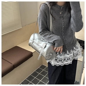 Close-up of a metallic silver barrel shoulder bag with adjustable straps on a casual outfit