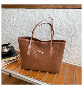 Detail of leopard print tote bag featuring a golden bow metal clasp on a wooden bench