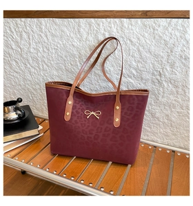 Detail of dark red leopard embossed tote bag with gold bow and brown leather handles