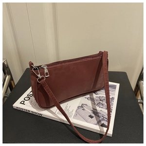 Détail d'un sac baguette bordeaux en nylon avec fermeture éclair argentée sur un livre