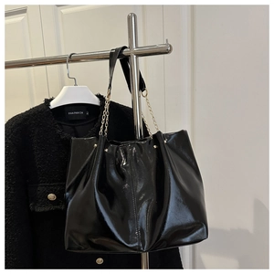 Macro view of shiny black leather tote featuring gathered pleats and metal chain strap