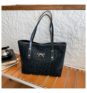 Detail of black leopard print tote bag featuring a decorative gold bow hardware pendant