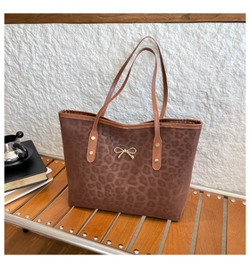 Close-up of leopard print tote bag with gold bow charm on a wooden bench