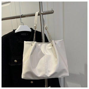 Close-up of white glossy tote bag featuring metal chain and leather spliced shoulder strap