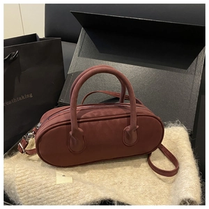 Detail of burgundy faux suede cylinder handbag featuring silver zipper and dual handles