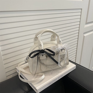 White patent leather Boston bag with black ribbons and silver chains on a book