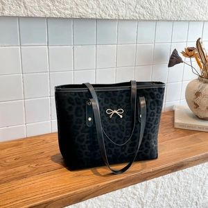 Chic black leopard print tote bag with golden bow accent on a wooden surface