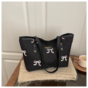 Close-up of black quilted tote bag with colorful bow embroidery and brand label
