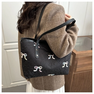 Detail of black quilted tote bag with colorful embroidered bows worn on the shoulder