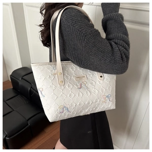 Detailed view of white quilted tote bag with colorful butterfly embroidery and metal logo