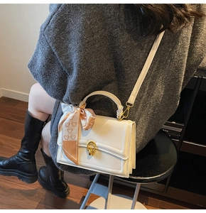 Dettaglio della borsa in pelle crema con chiusura girevole dorata e foulard di seta sul manico