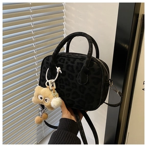 Detail of black leopard texture handbag with round handles and yellow plush charm