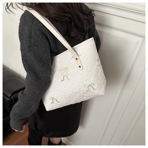 Detail view of white quilted tote bag with embroidered bows on a model's shoulder